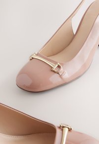 Rosa Slingback-Pumps aus Lackleder mit abgerundetem Zehenbereich, goldfarbenem Schnallendetail vorne und einem eleganten, glänzenden Finish.
