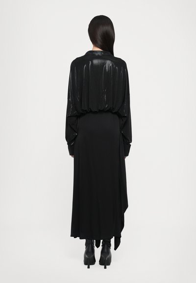 Long black dress with shiny textured sleeves, loose fit, and asymmetrical hem. Styled with black high-heeled boots.