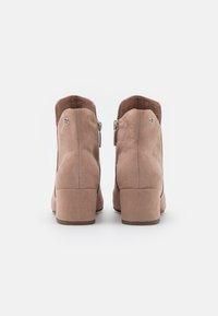 Beige Wildleder-Stiefeletten mit einem kurzen Blockabsatz, seitlichem Reißverschluss und glatter Textur. Runde Zehenform mit metallischem Akzent.
