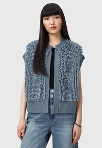 Gilet grigio a maglia con pannelli testurizzati e soffici sulle spalle, orlo a costine e senza maniche, indossato sopra una maglietta scura, abbinato a jeans in denim chiaro.