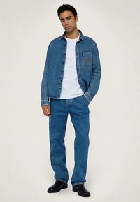 Jeansjacka i ljusblått med en bröstficka, kombinerad med matchande jeansbyxor. Bärs över en vit t-shirt och svarta stövlar.