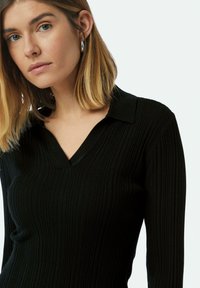 Schwarz geripptes langärmeliges Oberteil mit V-Ausschnitt und Kragen-Design, das aus einem strukturierten Stoff gefertigt ist und eine figurbetonte Silhouette bietet.