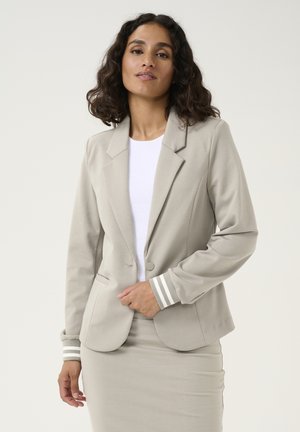 Blazer aderente grigio chiaro con chiusura a un bottone, rever su misura e polsini a righe, abbinato a una gonna coordinata. Tessuto con una texture morbida.