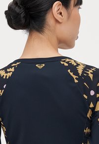 Rash guard featuring a black body with gold and pink abstract patterns on the sleeves. Smooth texture and a small logo at the neck.