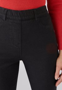 Jeans negros de cintura alta con una cinturilla elástica, bolsillos frontales y una textura suave. La tela es de mezclilla y presenta un diseño clásico.