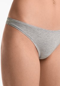 Grijze katoenen string met dunne zijkanten, gladde textuur en minimalistisch ontwerp. Stiksels zichtbaar langs de randen.