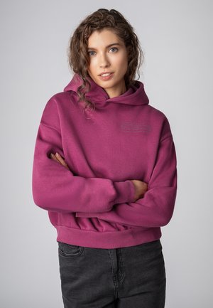 Fuchsia Sweatshirt mit Kapuze, im lockeren Schnitt und mit gerippten Bündchen, kombiniert mit dunkelgrauen Hosen. Mit einem bedruckten Logo-Detail auf der Vorderseite.