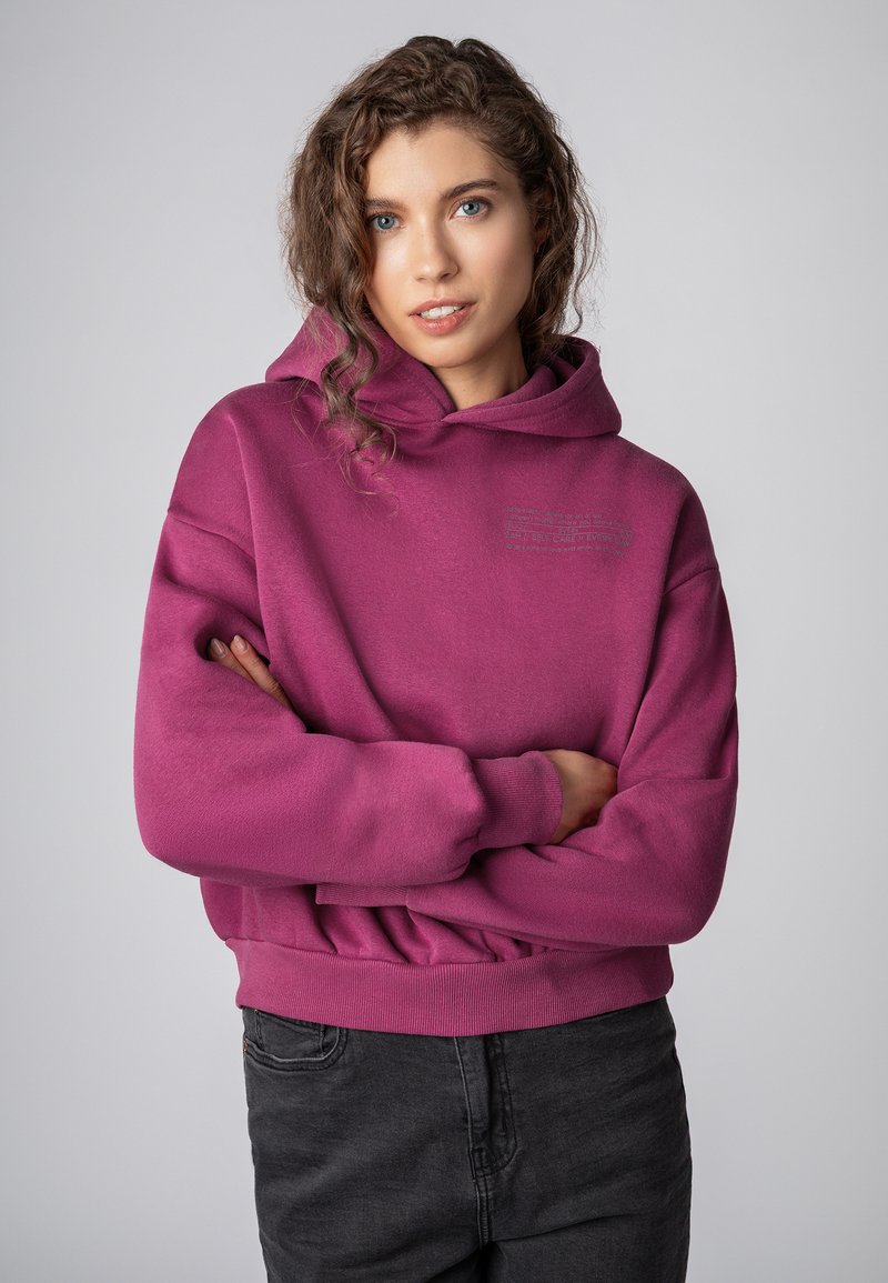 Fuchsia sweatshirt met een capuchon, voorzien van een relaxte pasvorm en geribbelde manchetten, gecombineerd met donkergrijze broek. Bevat een gedrukte logodetail aan de voorkant.