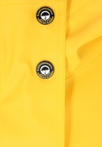 Gul vattentålig tyg med två svarta knappar som har en paraplydesign och text. Slät yta och sydda kanter.