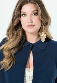 Navyblauer Cardigan mit Kragen, der eine Frontöffnung und eine weiche Textur aufweist. Auffällige goldene Statement-Ohrringe sorgen für visuelles Interesse.
