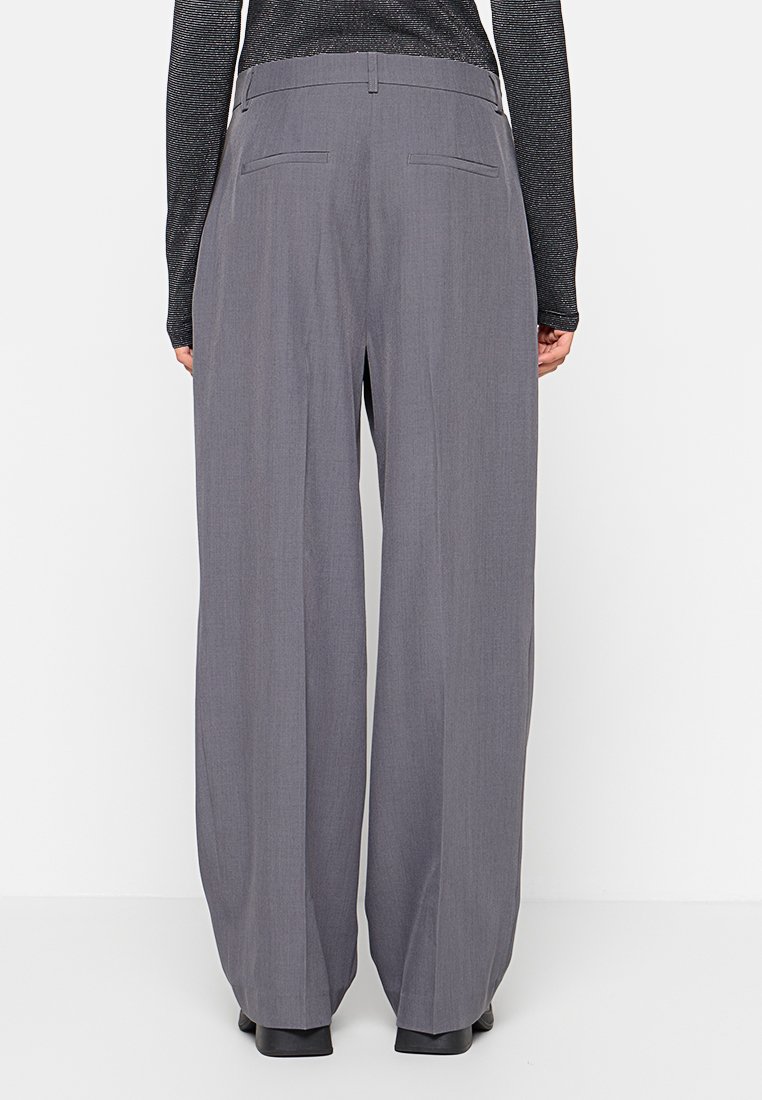 Graue, weit geschnittene Hosen von hinten betrachtet, mit einem strukturierten Stoff, zwei Gesäßtaschen und einem hohen Bund.