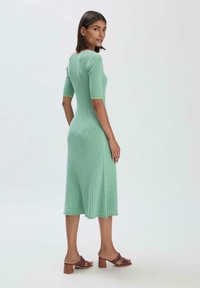 Geripptes, mintgrünes Midikleid mit kurzen Ärmeln, figurbetontem Schnitt und ausgestelltem Saum. Akzentuiert mit einem kontrastierenden Ärmeldetail.