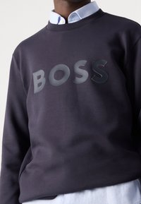 Marinblå sweatshirt med rundhals, prydd med en glänsande "BOSS"-logotyp över bröstet. Tyget ser slätt ut med en avslappnad passform.