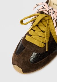 Καφέ σουέτ αθλητικά παπούτσια με μαύρες πατωμένες λεπτομέρειες, κίτρινες και ροζ κορδόνια, �χρυσά άκρα κορδονιού και ανθεκτική υφή σόλα.