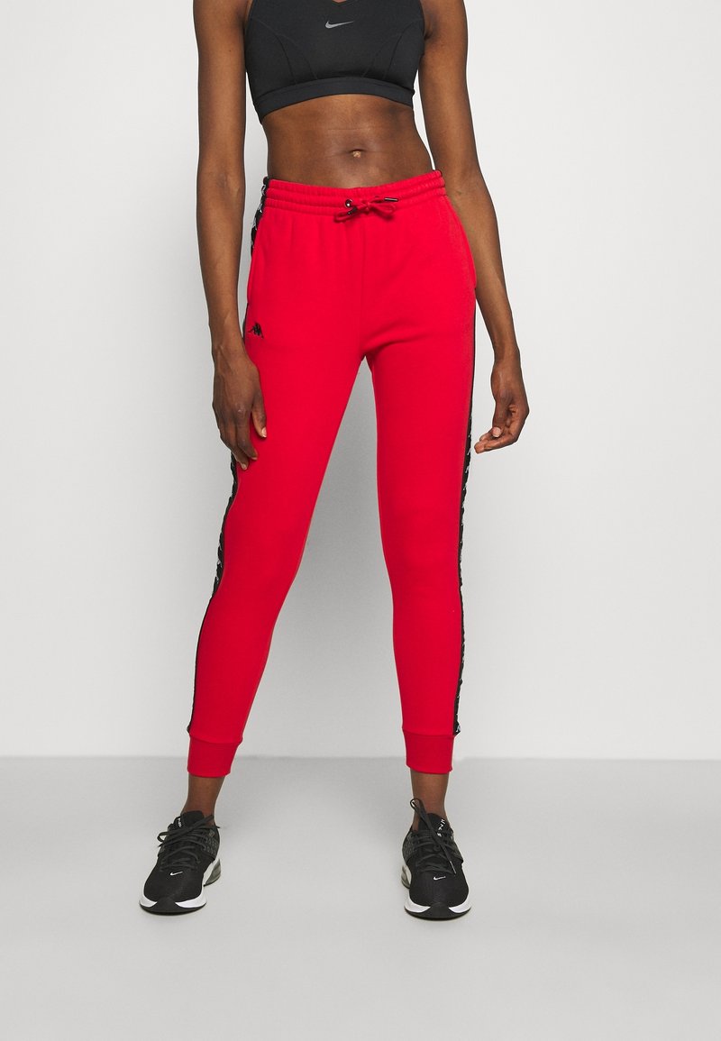 Rode sportieve broeken met zwarte zijstrepen, elastische tailleband en boorden. In combinatie met zwarte sneakers, die een strak ontwerp en materiaal hebben.