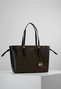 Zwarte en bruine leren tote bag met gouden hardware, voorzien van een monogrampatroon, dubbele handgrepen en een hangende logo charm.