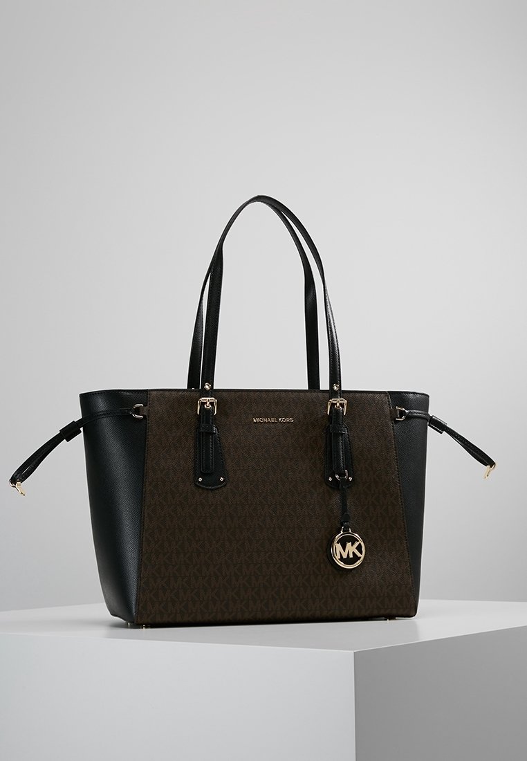 Zwarte en bruine leren tote bag met gouden hardware, voorzien van een monogrampatroon, dubbele handgrepen en een hangende logo charm.