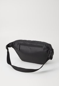 Zwarte nylon schoudertas met een gewatteerde textuur, verstelbare schouderband en een ritsvak aan de achterkant. Compacte, rechthoekige vorm.