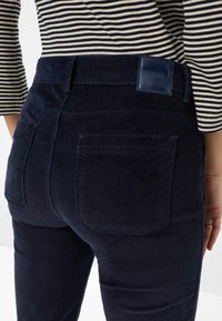 Marine corduroy broek met een gladde textuur, voorzien van achterzakken en een leren label. Gekleed met een gestreepte langemouwen top.