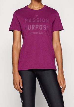 Camiseta de algodón morada con mangas cortas, que presenta un atrevido estampado gráfico en negro que dice "PASSION PURPOSE Project Roc" en la parte delantera.
