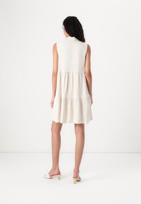 Robe sans manches beige avec un design en étages, faite de tissu léger. Elle présente un col et une silhouette fluide.
