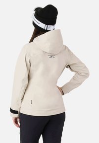 Giacca impermeabile beige con cappuccio, caratterizzata da un logo nero sul retro, dettagli neri sulle maniche e un design aderente.