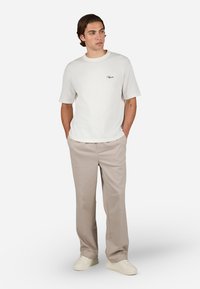 Hvid ribbet kortærmet t-shirt med rund halsudskæring og sort broderet logo, parret med beige lige ben bukser og hvide sneakers.