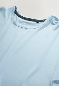 T-shirt de sport bleu clair respirant avec col rond et petites perforations dans le tissu pour la ventilation.