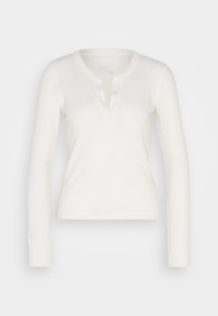 Vit, långärmad topp i ribbad struktur med djup V-ringning och treknapppslå. Mjuk textur och figurnära design. Ärmsluten är ribbade.