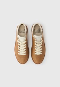 Καφέ δερμάτινα αθλητικά παπούτσια με κρεμ κορδόνια, λευκή γλώσσα και λαστιχένιες σόλες. Διαθέτουν ραφές λεπτομέρειας και ανάγλυφο λογότυπο στην πάτο.