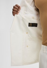 Weißes Blazer-Innenfutter mit glatter Textur, Manteco-Label, Knopfverschluss und einer Innentasche mit hellblauem Rand.