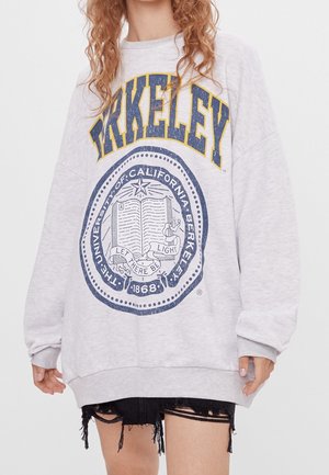 Sweatshirt gris oversize avec "BERKELEY" en lettres bleues et jaunes, accompagné d'un graphisme du sceau de l'université en bleu marine sur le devant.