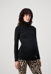 Fekete, hosszú ujjú, nyakba húzott felső, oldalán ráncolással, bézs leggings-szel párosítva, fekete, hullámos zebra mintával. Simább, rugalmas anyag.