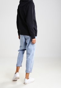 Černá mikina s kapucí, volné světlé modré džínové kalhoty se zahnutými nohavicemi u kotníků, kombinované s bílými teniskami. Jednoduchý design a pohodlný střih.