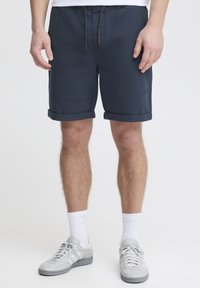 Mørkeblå shorts med oppbrettede ermer, elastisk liv og snøring. Kombinert med lysegrå sporty joggesko og hvite ankelstrømper.