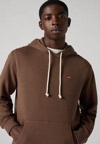 Felpa con cappuccio marrone realizzata in materiale morbido, dotata di tasca frontale, stringhe bianche e un piccolo logo rosso di Levi's.