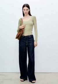 Top a coste verde oliva attillato, jeans a gamba larga in denim scuro con vita con lacci e borsa marrone. Texture lisce, dettagli minimi.