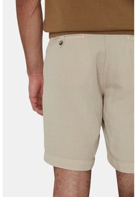 Shorts in lino color beige con orli arrotolati, dotati di una singola tasca posteriore con chiusura a bottone e dettagli di cucitura visibili.