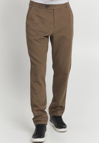 Brown cotton trousers with a straight-leg fit, featuring a button closure and belt loops, paired with black sneakers.