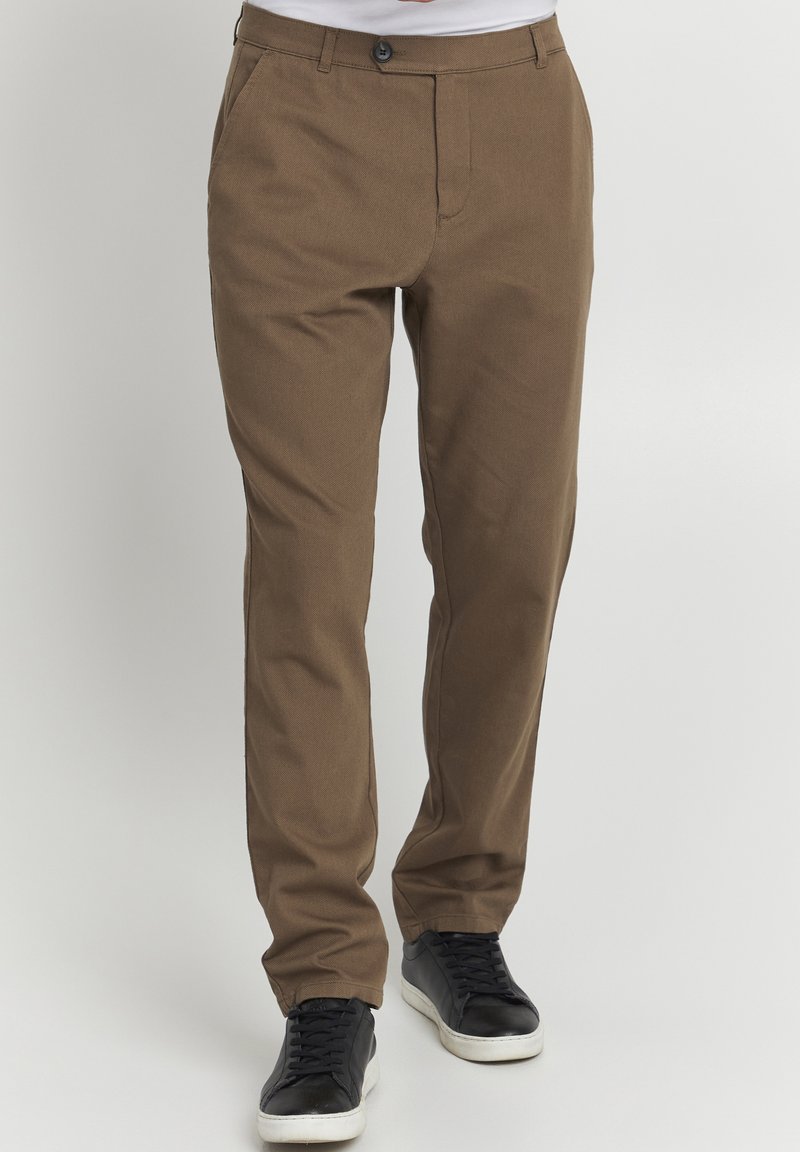 Brown cotton trousers with a straight-leg fit, featuring a button closure and belt loops, paired with black sneakers.