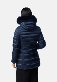 Kurtka puchowa w ciemnym granacie z poziomym wzorem pikowania, z futrzanym kapturem i zapięciem na zamek. Posiada dopasowany krój oraz gładką, błyszczącą strukturę.