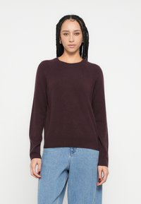 Pulover tricotat burgundy cu mâneci lungi, guler rotund și bordură cu nervuri; asortat cu blugi din denim albastru deschis. Textură moale, design simplu.