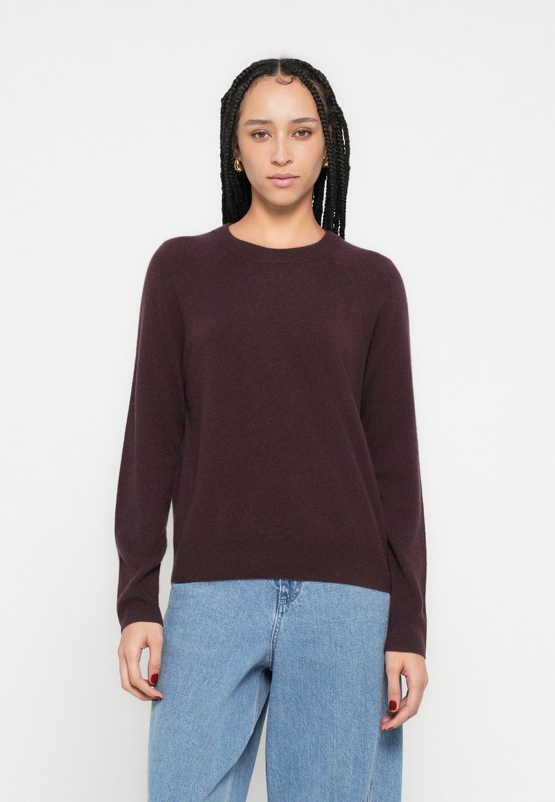 Pulover tricotat burgundy cu mâneci lungi, guler rotund și bordură cu nervuri; asortat cu blugi din denim albastru deschis. Textură moale, design simplu.