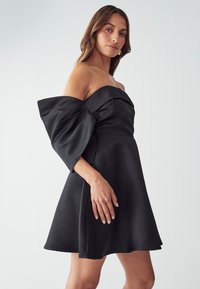 Musta satiini off-the-shoulder -mekko, jossa on pullistetut hihat, vartalonmyötäinen yläosa ja leveä helma. Sujuva pinta ja virtaviivainen siluetti.