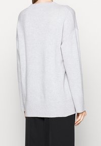 Pull oversize gris clair avec un ourlet et des poignets côtelés. Fabriqué en matériau doux avec des épaules tombantes et une coupe décontractée. Aucun motif visible.