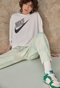 Camiseta blanca de gran tamaño con el logo negro de Nike, combinada con pantalones de chándal en tie-dye verde pastel. Zapatillas verdes y blancas con detalles en azul.