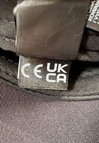 Étiquette de vêtement montrant les marques de certification CE et UKCA cousues à l'intérieur d'un vêtement en tissu noir.