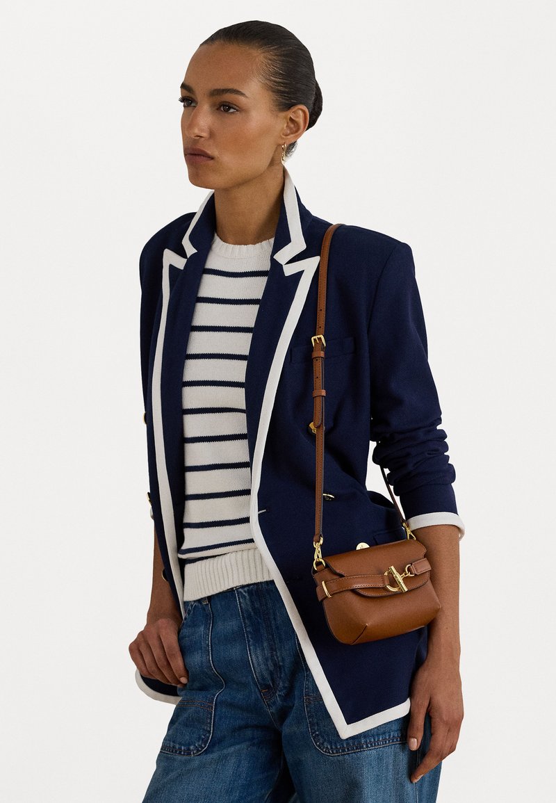 Sötétkék blézer fehér díszítéssel, csíkos pulóver krém és sötétkék színekben, laza farmernadrág és egy kis barna bőrtáska arany kiegészítőkkel.