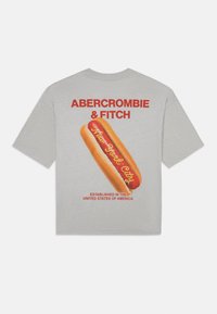 Camiseta gris de manga corta con un gráfico de un perrito caliente y "Nueva York" en amarillo, con "Abercrombie & Fitch" en rojo arriba.
