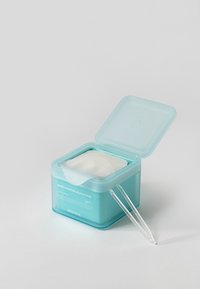 Boîte en plastique bleue avec couvercle ouvert contenant des tampons blancs pour imperfections et une petite pince transparente sur une surface blanche.